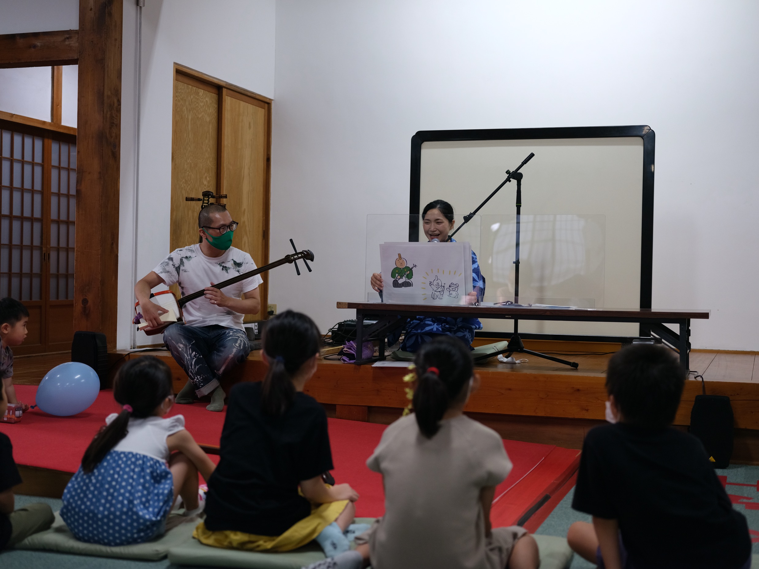 三味線を紹介するオリジナル紙芝居を語り部として活躍されている満茶乃さんに演じてもらい、それに合わせて演奏する筆者　Photo by Makoto Watanabe