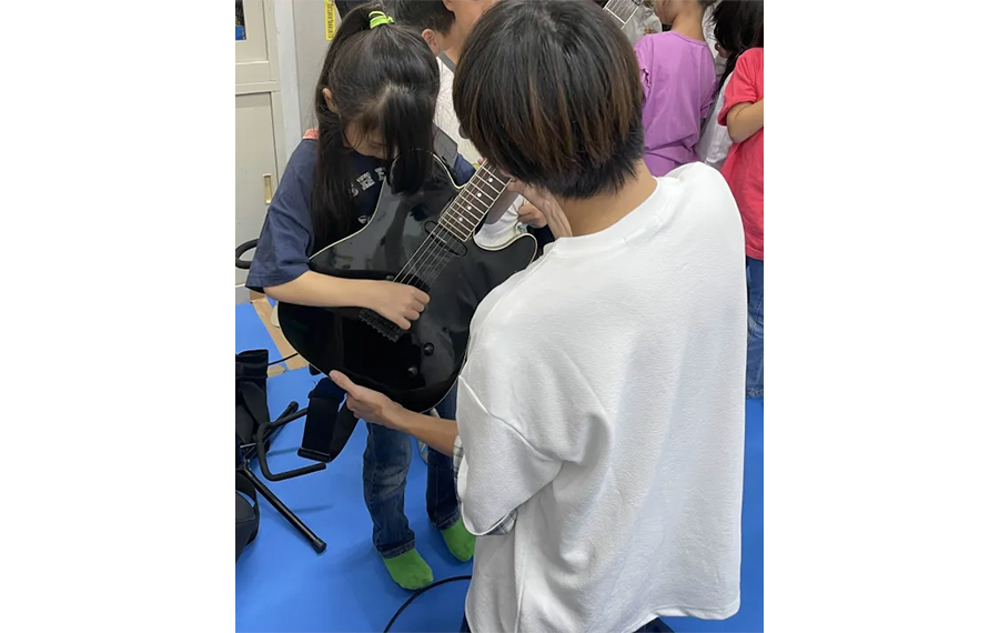 児童クラブでの楽器体験の様子。学生が楽器を手渡しながら説明。
